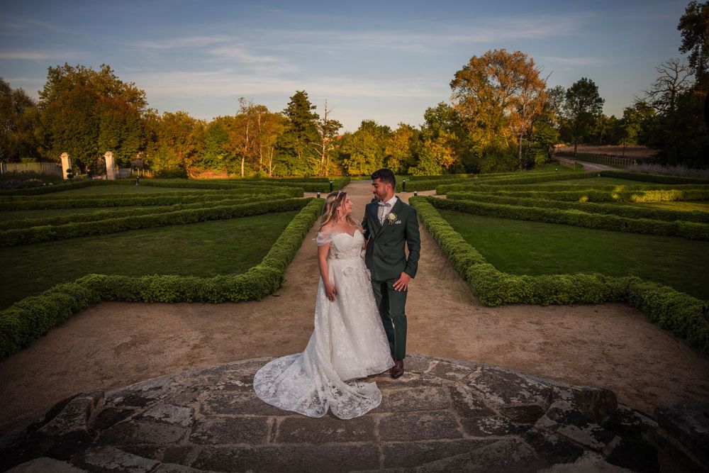 A couple walks through a scenic garden path during golden hour sunset at a formal estate property.