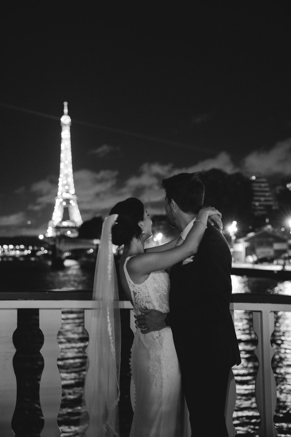 Bride and groom embrace near the Eiffel Tower at night in Paris, black and white wedding photo.