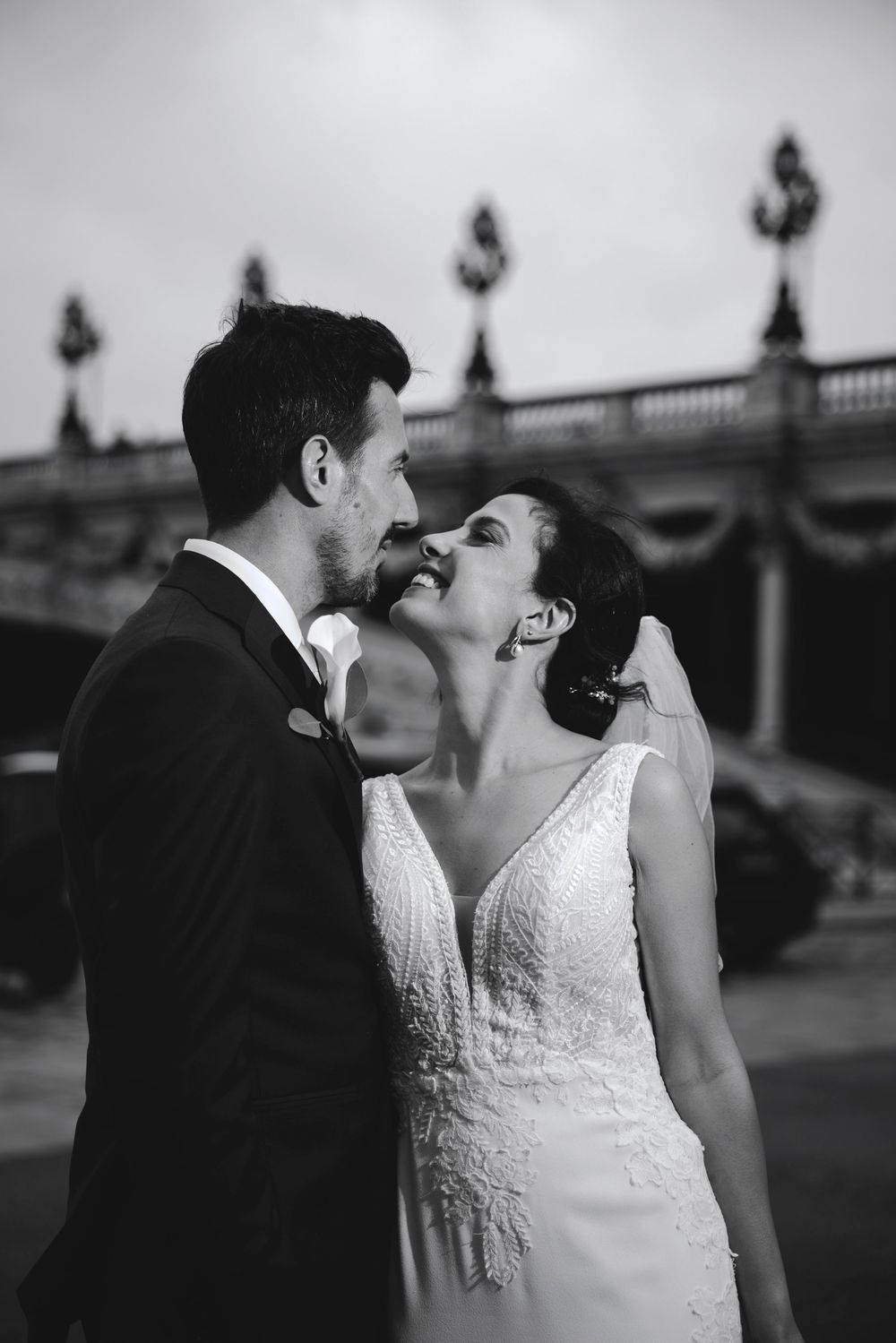 Black and white photo of a bride and groom sharing a romantic moment near an ornate bridge in Paris.