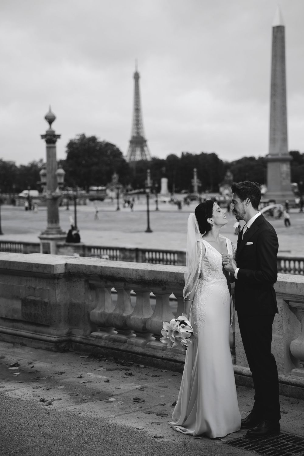 Black and white photo of a bride and groom kissing in Paris with the Eiffel Tower in the background.