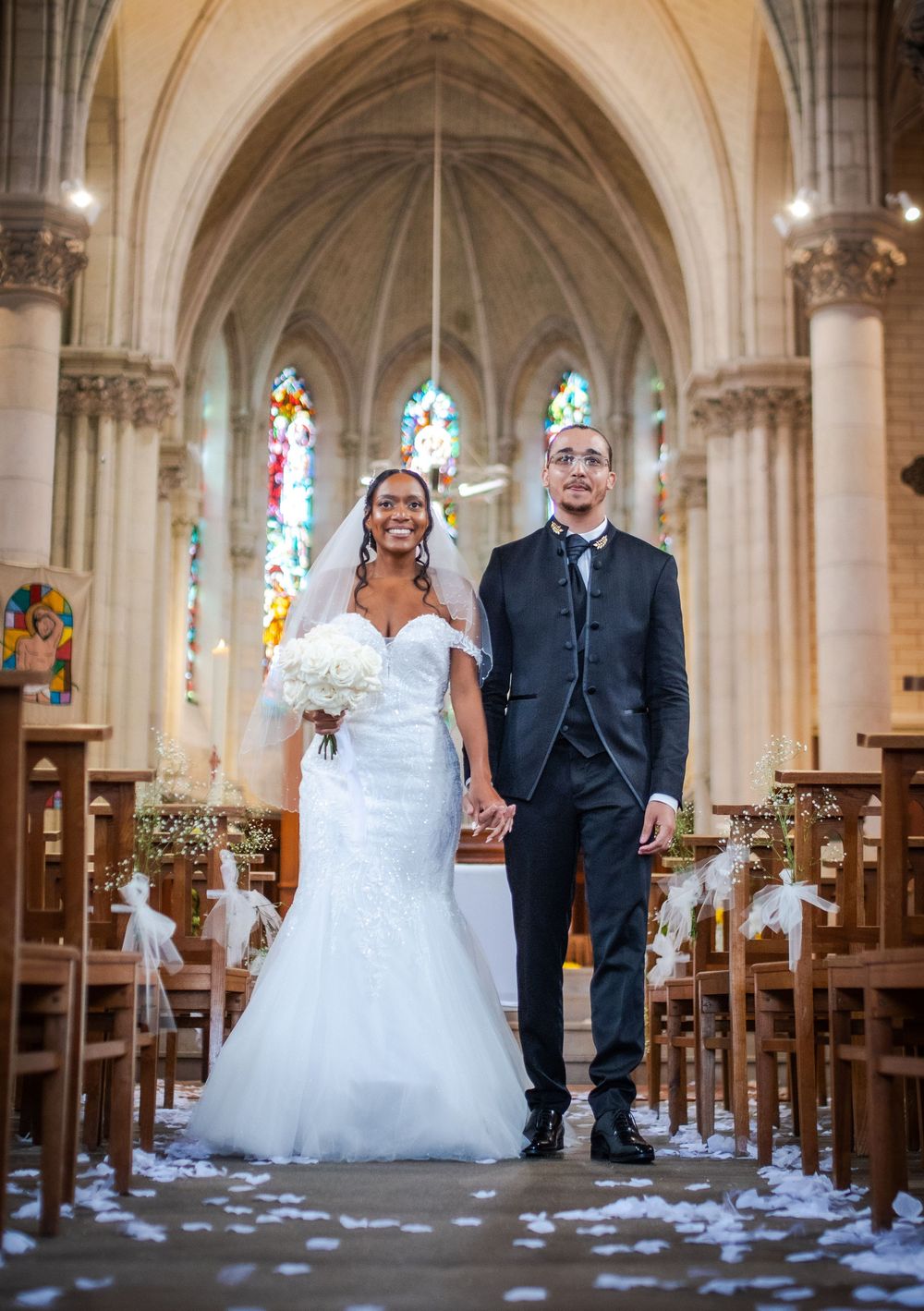 A joyful wedding moment captured inside a beautiful gothic church with stained glass windows and scattered flower petals.