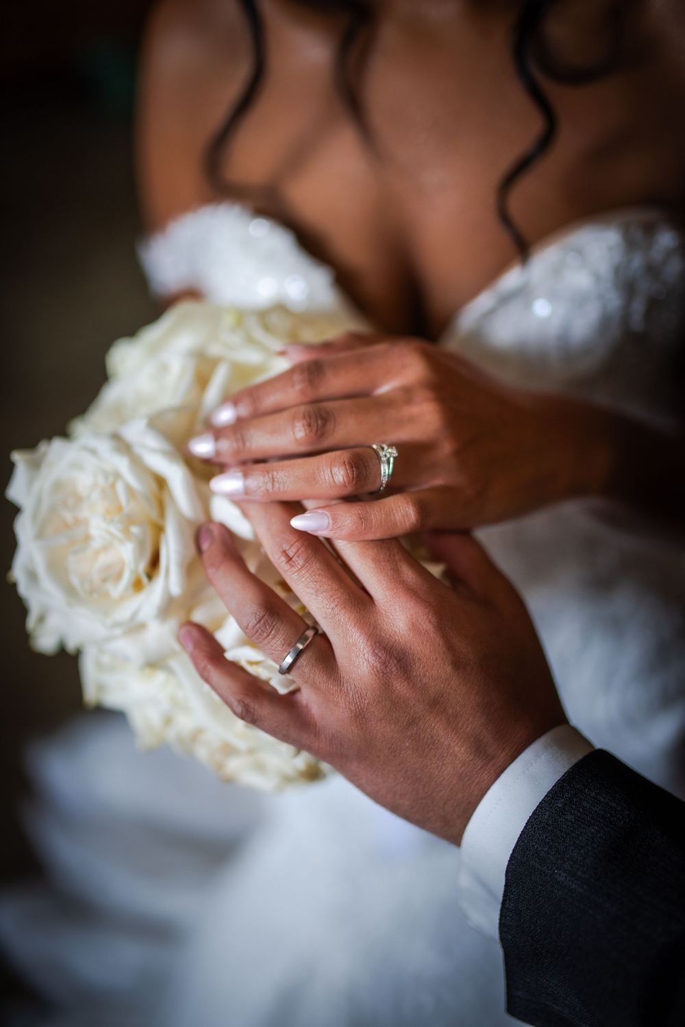 Close-up shots showing hands of a bride and groom holding a white wedding bouquet of roses during an intimate moment.