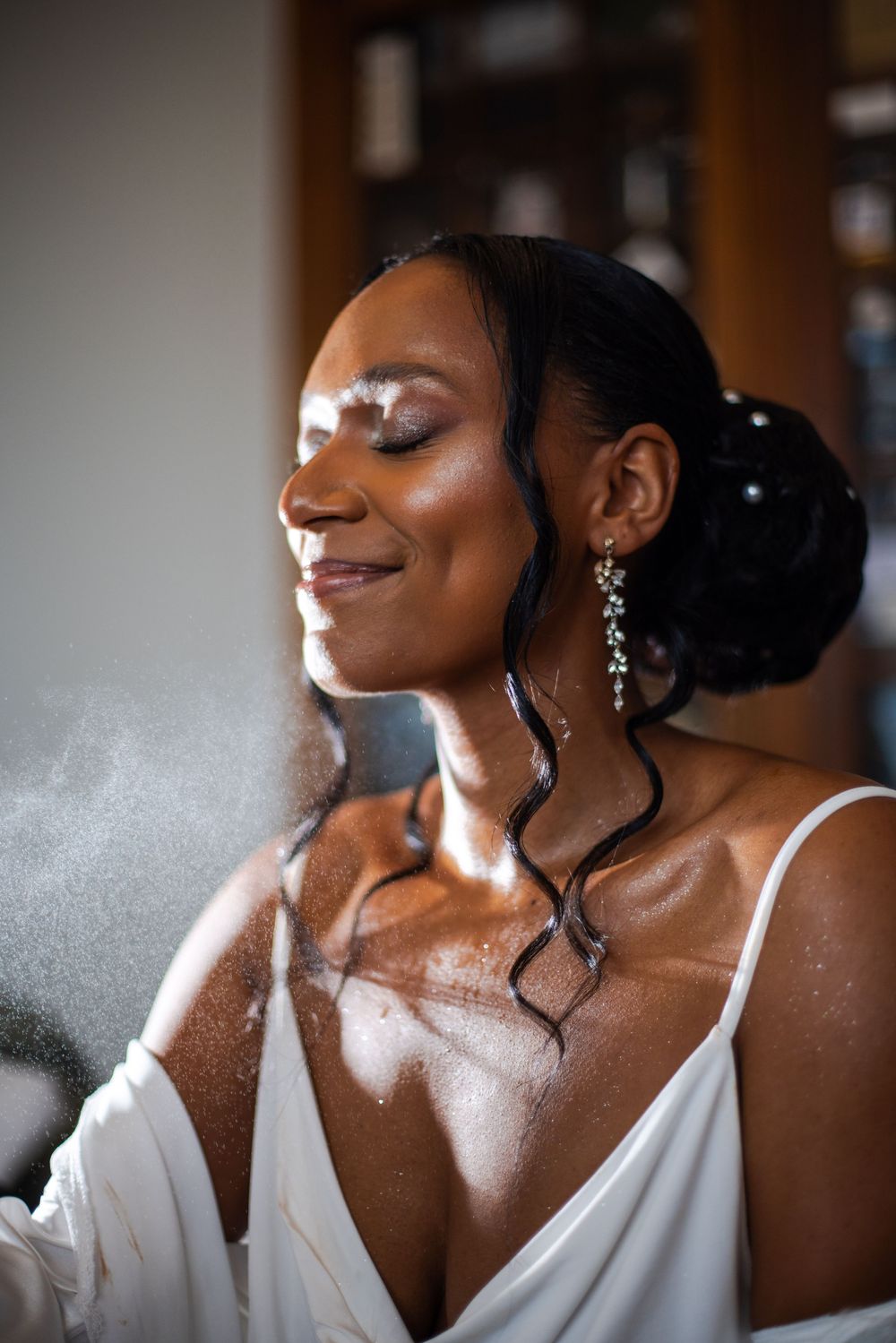 Close-up photo of a person wearing a white top with dramatic lighting and curled tendrils of hair.