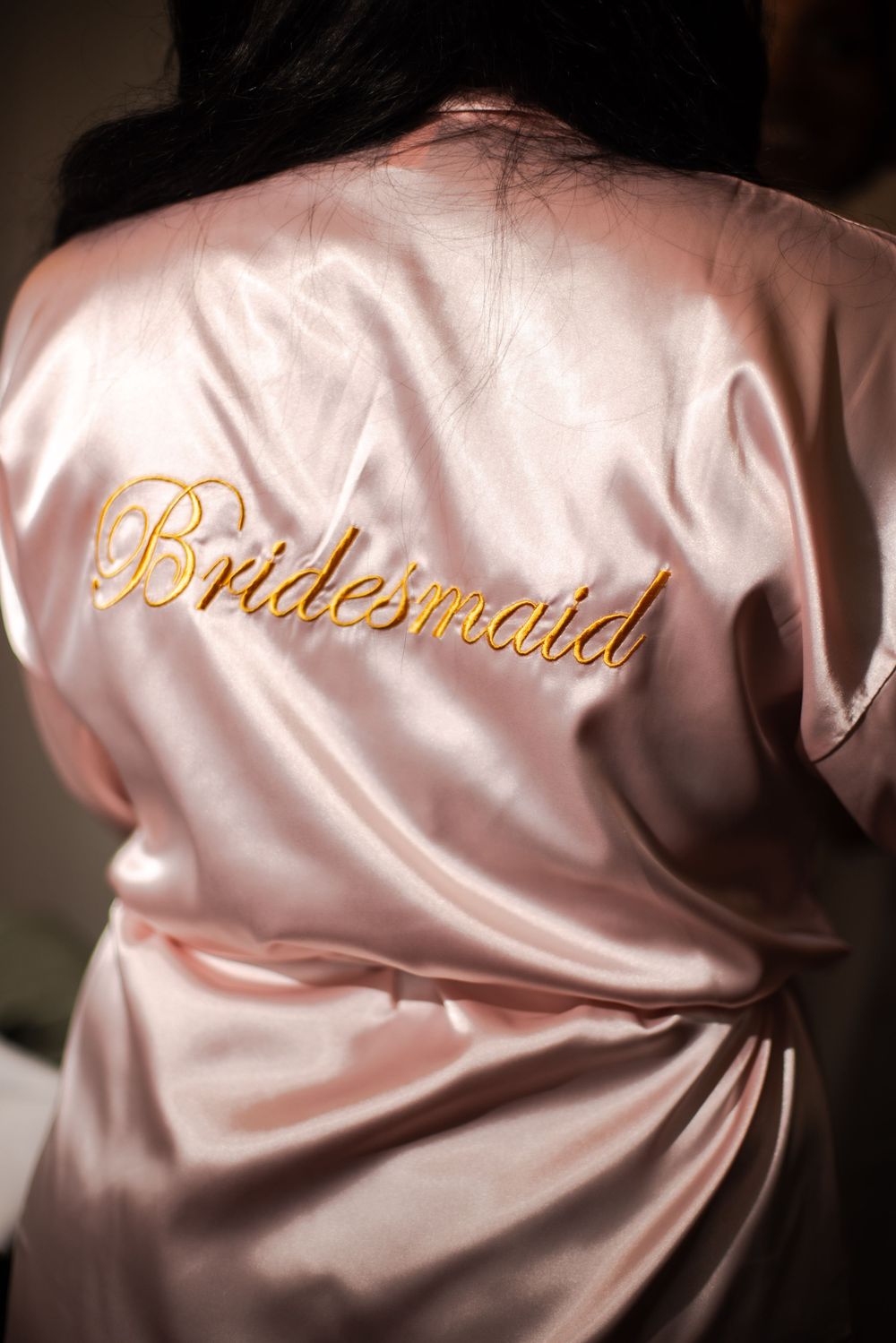 Pink silk or satin robes with gold 'Bridesmaid' embroidery text displayed in a row for a wedding party.
