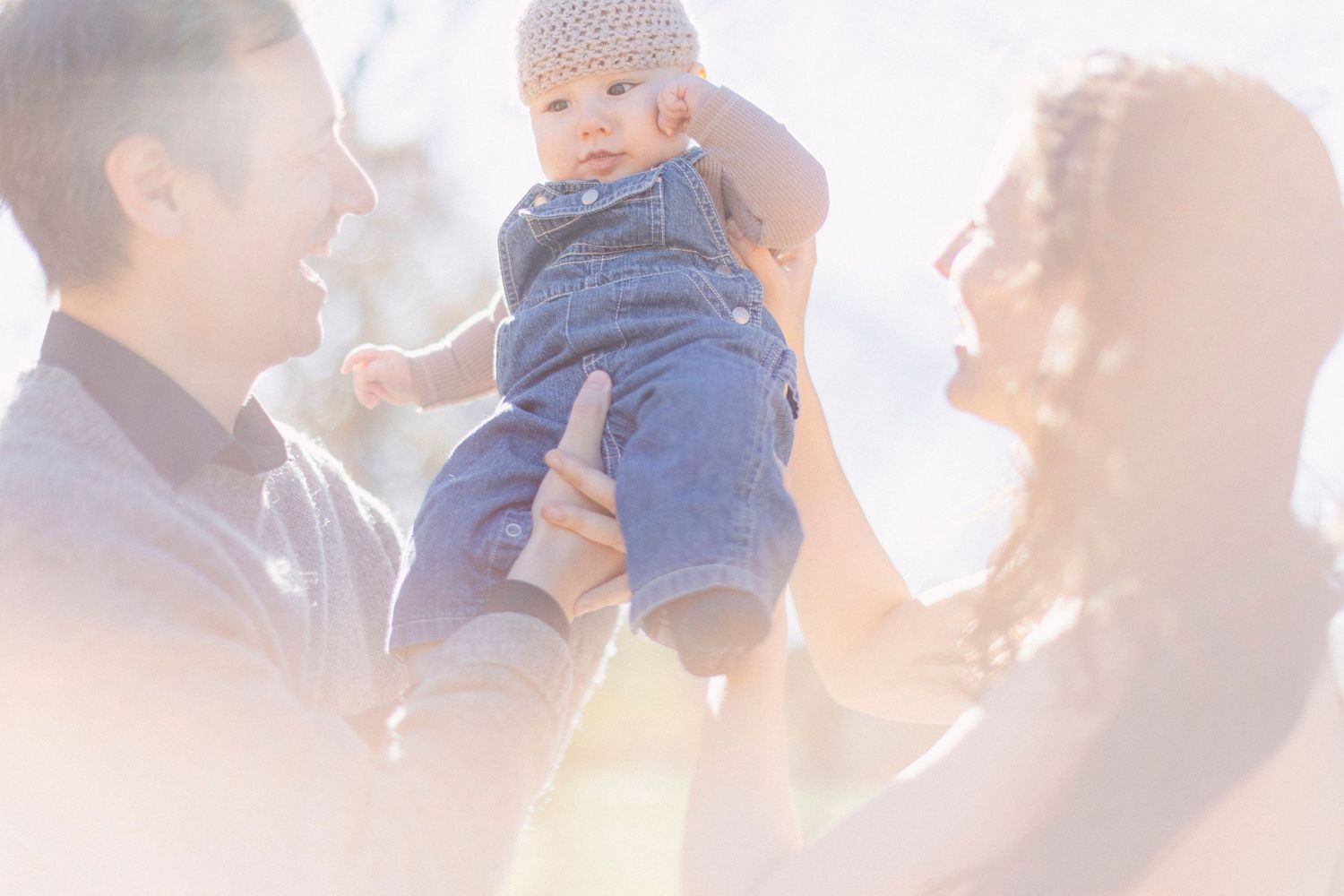 Family shares joyful moment lifting baby in sunlit outdoor setting.