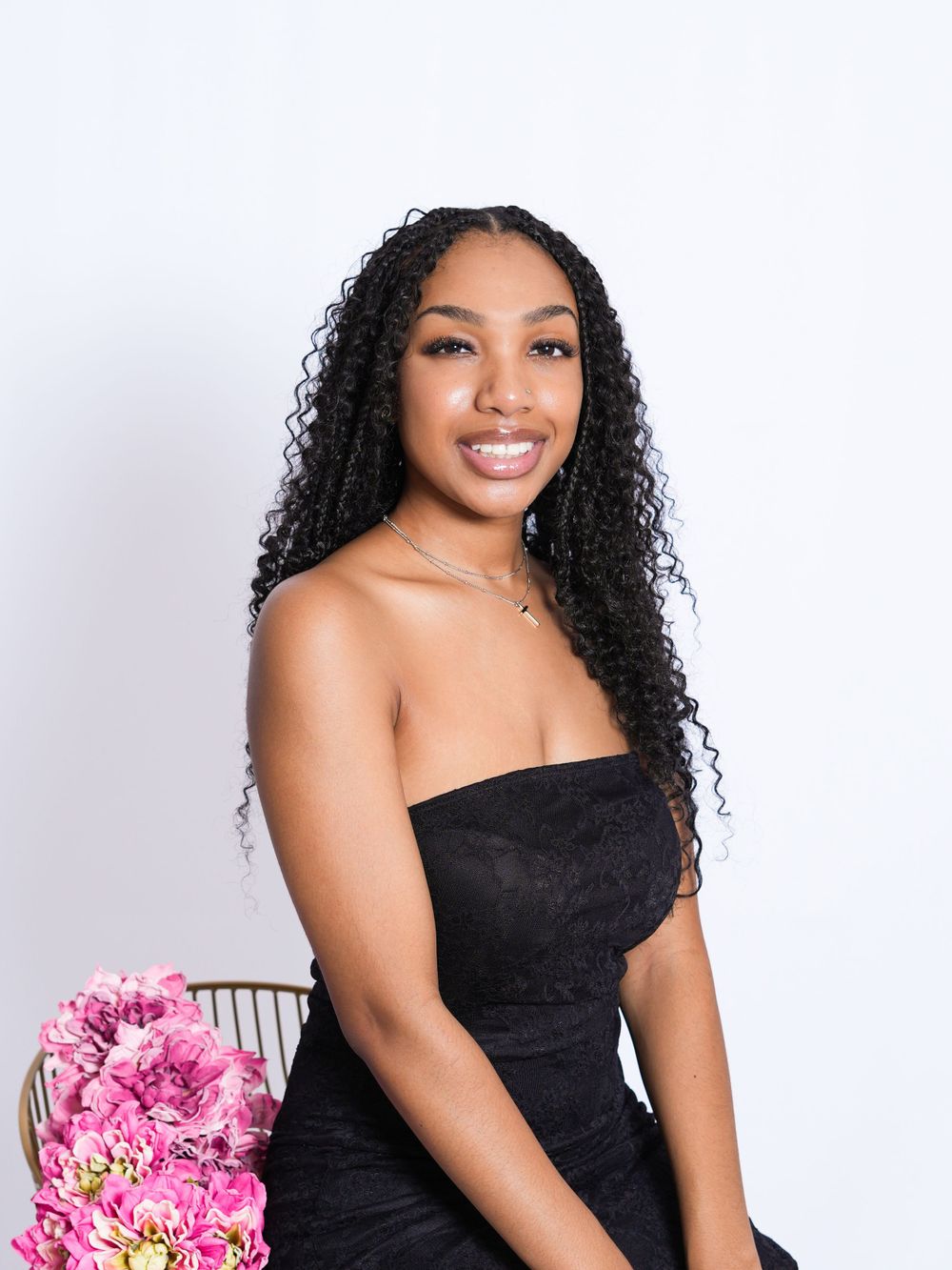 Portrait of person in black dress with curly hair and pink flowers against white background.