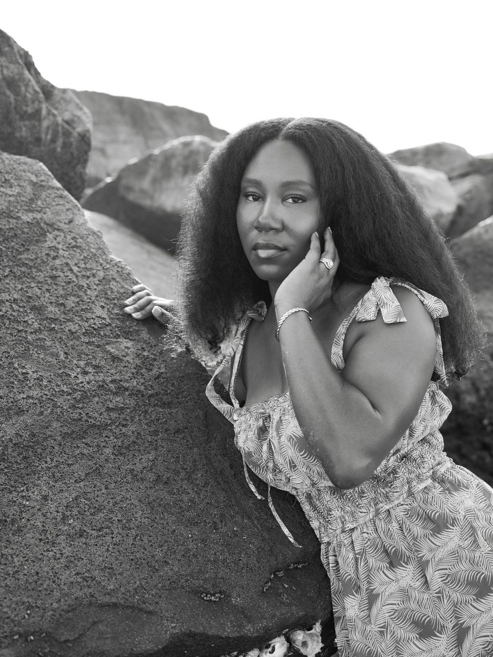 Portrait against dramatic coastal rocks showcasing natural curls and a patterned summer dress.