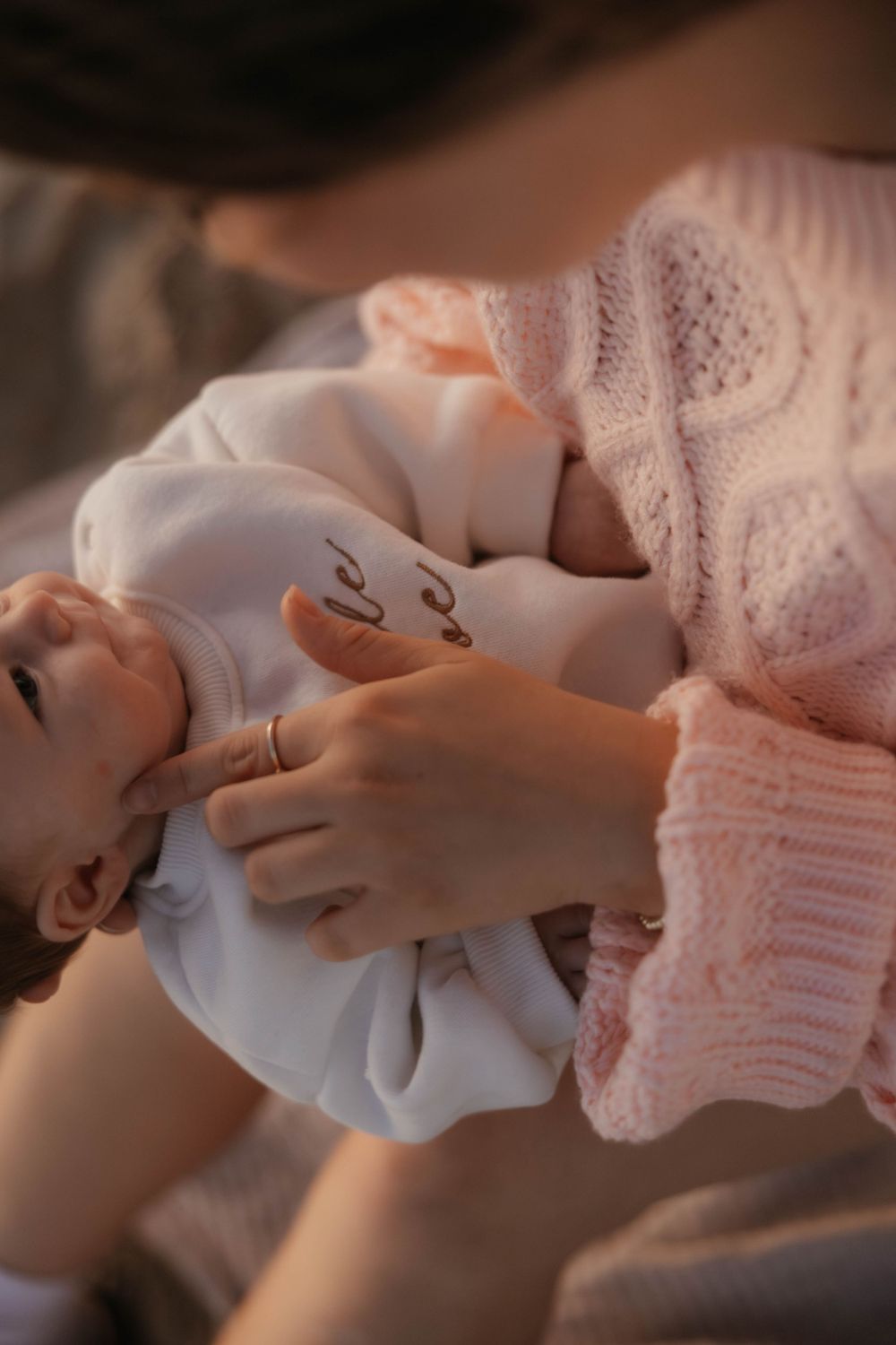 Close-up of mother in pink sweater cradling sleeping newborn baby outdoors.