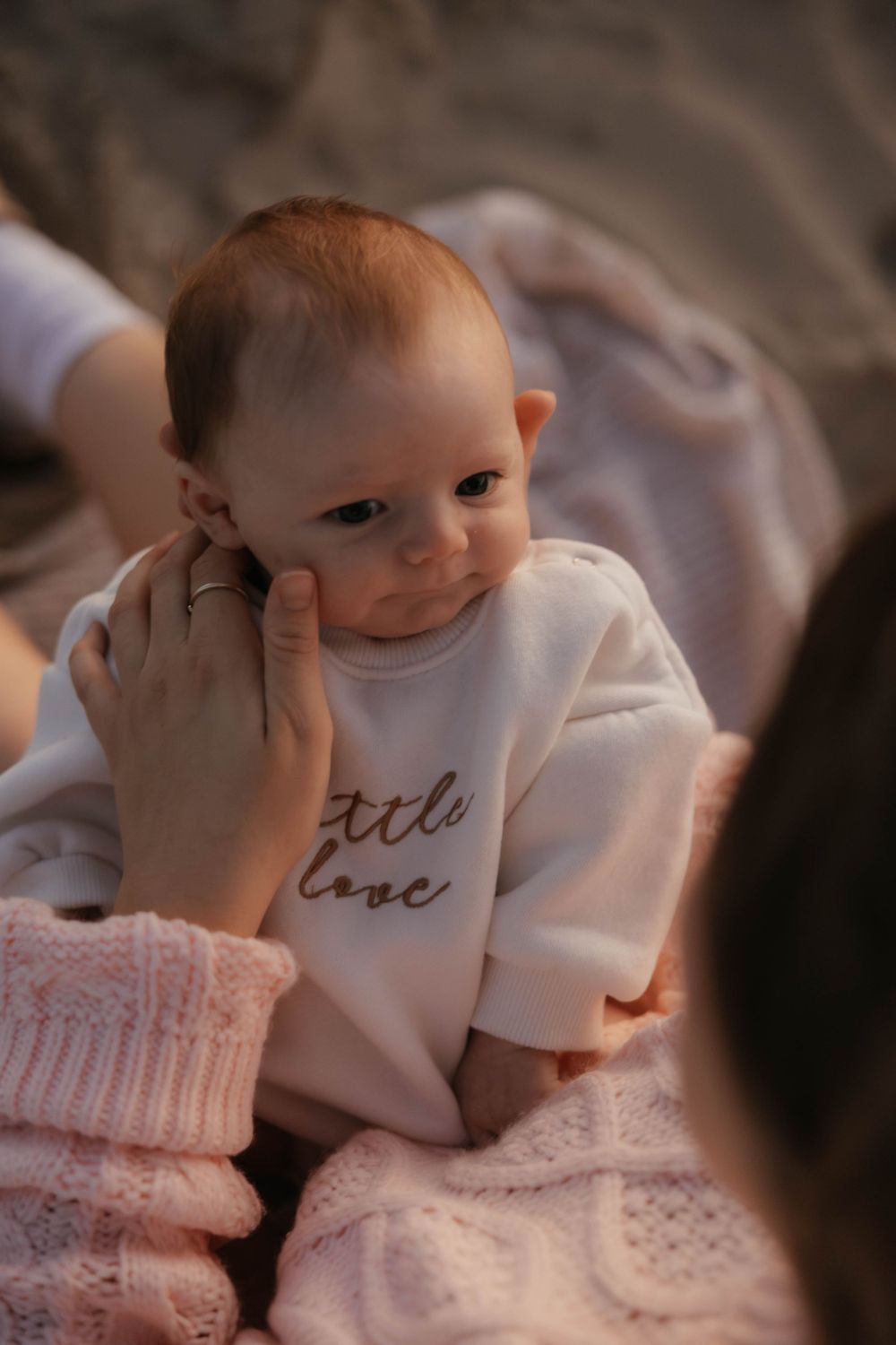 Close-up of newborn in little love onesie being cradled by mother on beach.