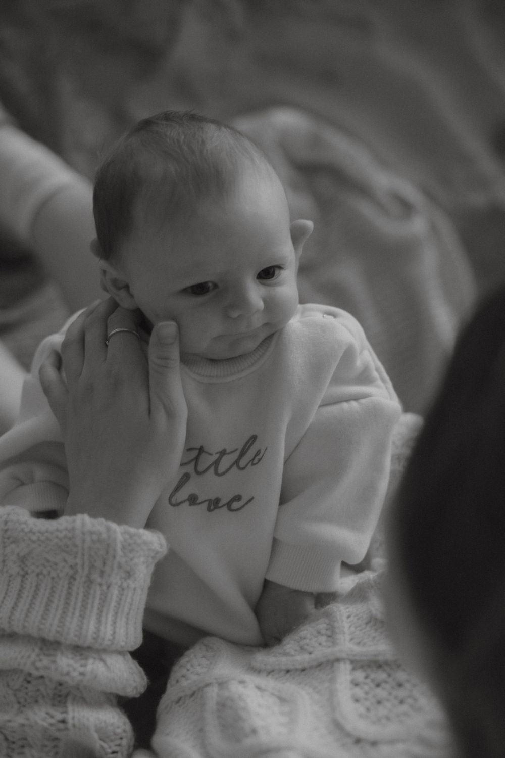 Black and white close-up of newborn in little love onesie held by mother.