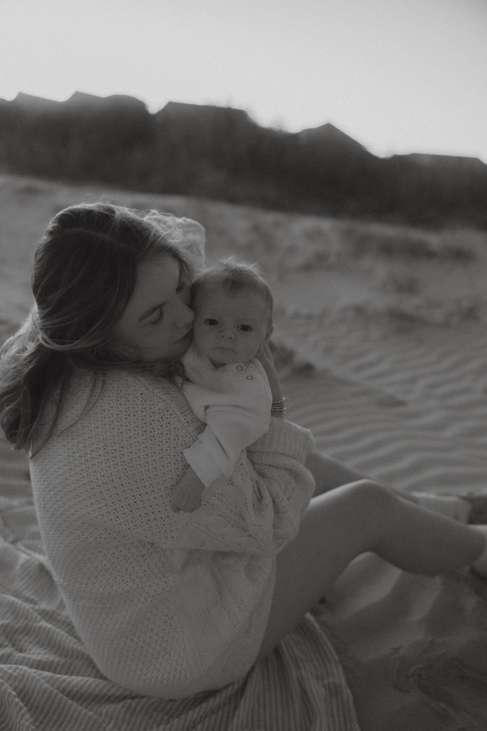 Black and white photo of loving mother cuddling newborn baby on sandy beach.