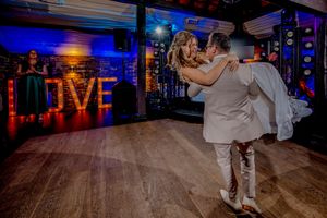 Wedding reception guests dancing on a wooden floor under blue and red mood lighting.