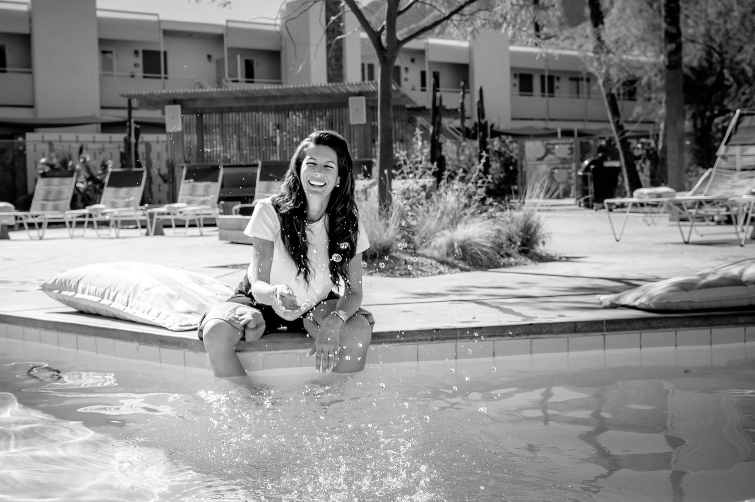 Black and white photograph of someone sitting by the edge of a swimming pool, splashing water with their feet.