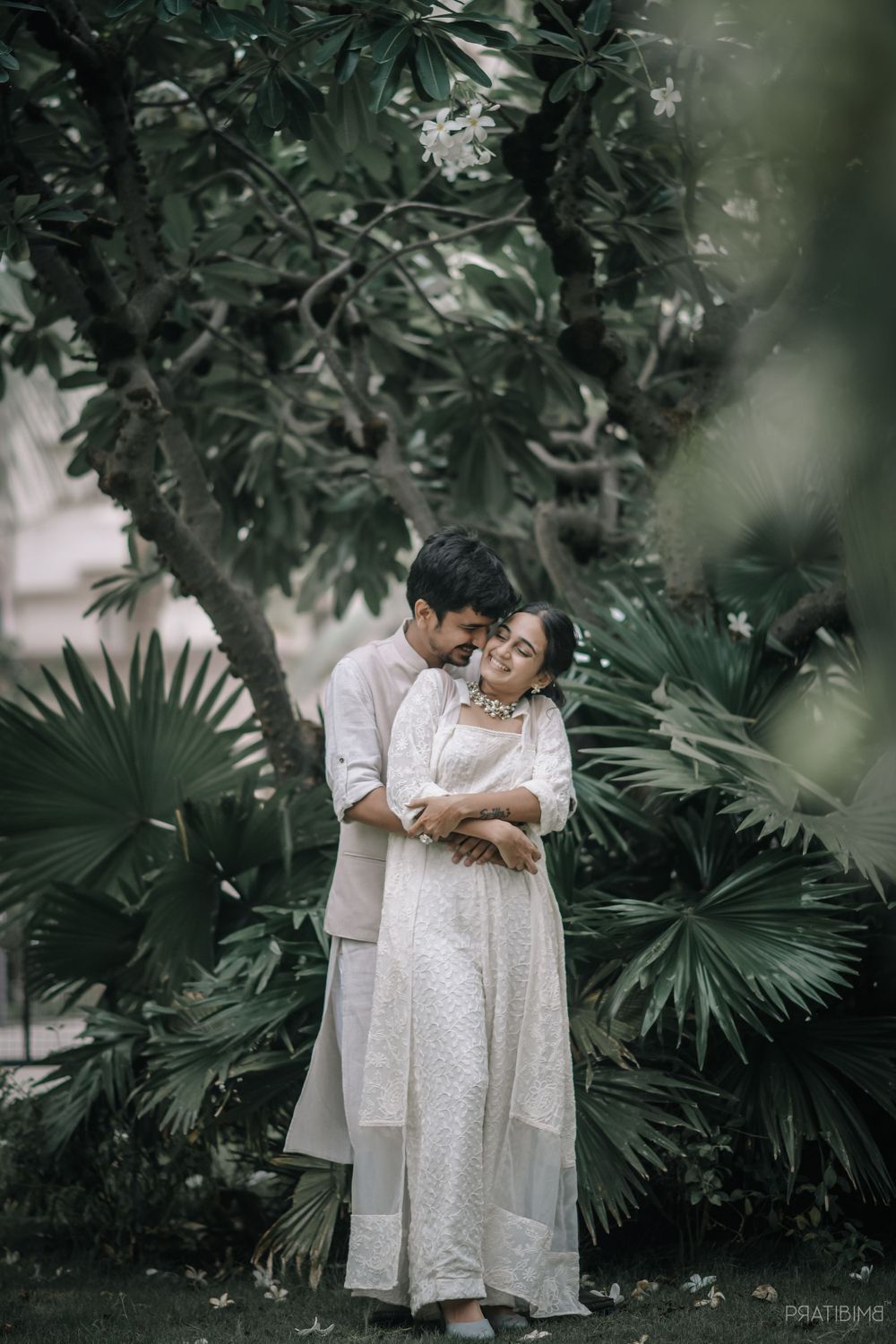 A couple in white and gray attire sharing a tender moment in a garden setting.