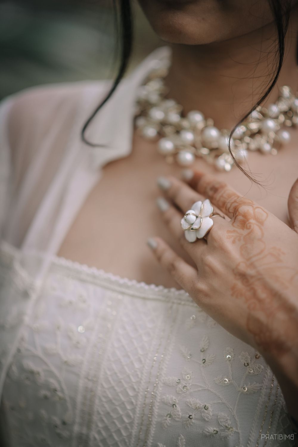 A close-up of a pearl necklace and floral ring on a white lace dress.