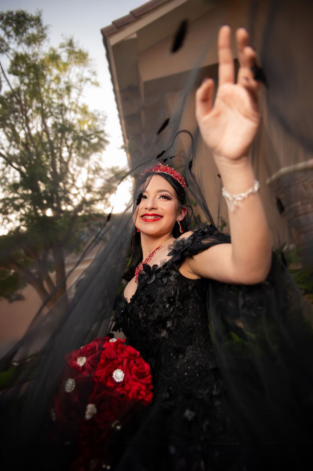 Bride in dramatic black wedding dress holding red bouquet with joyful expression at sunset.