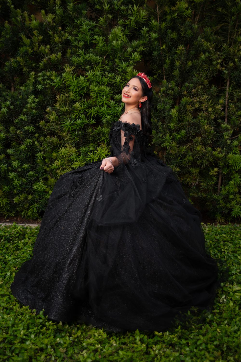 Elegant black ball gown with off-shoulder details shown against lush garden foliage.