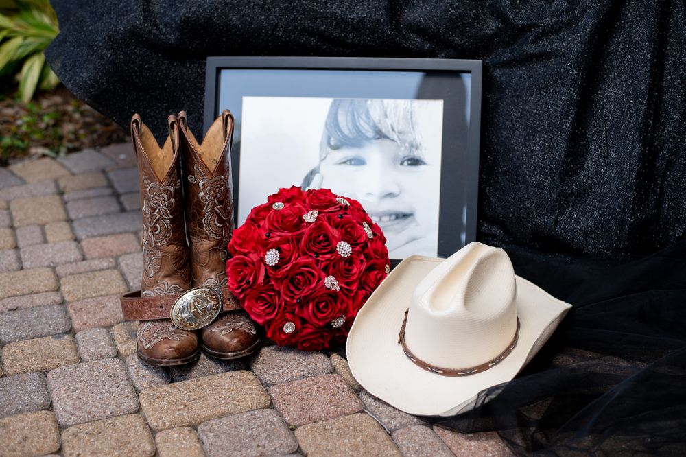 Cowboy boots, white hat, and red rose bouquet arranged on brick pavement.