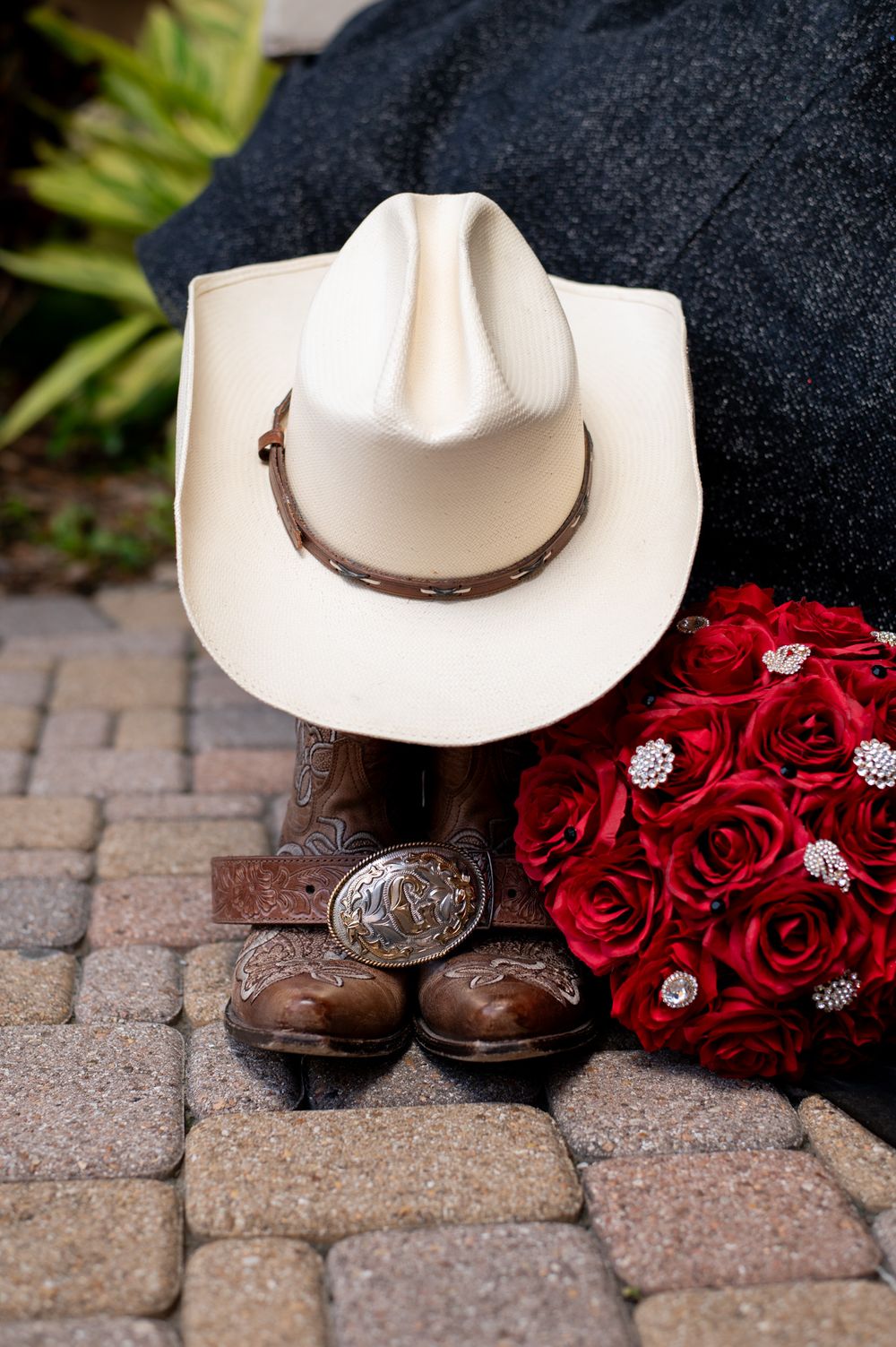 White cowboy hat, leather boots and red rose bouquet styled on brick pavers.