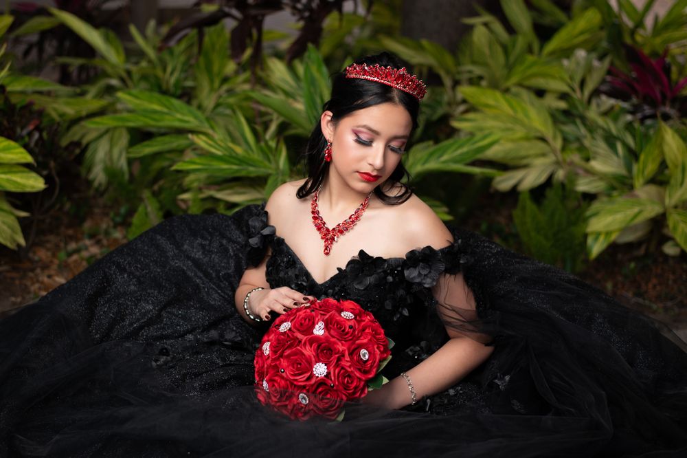 Black ball gown with red accessories photographed in garden setting.