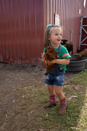 Toddler plays outside red barn wall in summer during candid photo sequence.