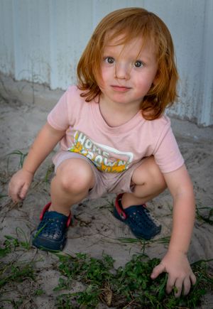 Child exploring plants and dirt while crouching down.