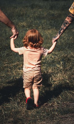 Person helping toddler walk on grass in warm sunset lighting.