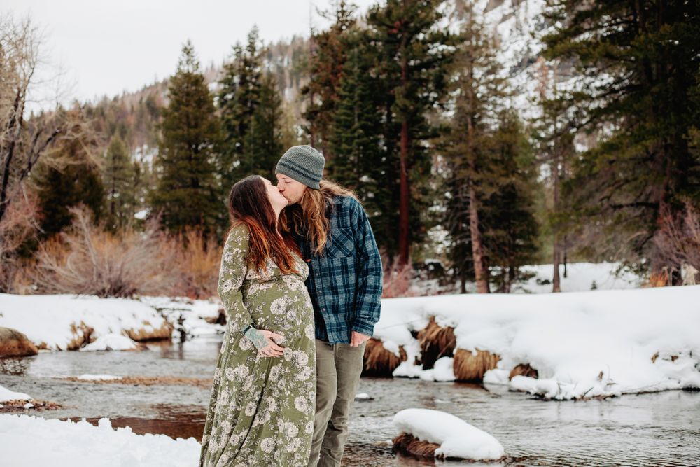 winter maternity portrait of pregnant mom and her partner kissing and walking along a snow covered river in Lake Tahoe