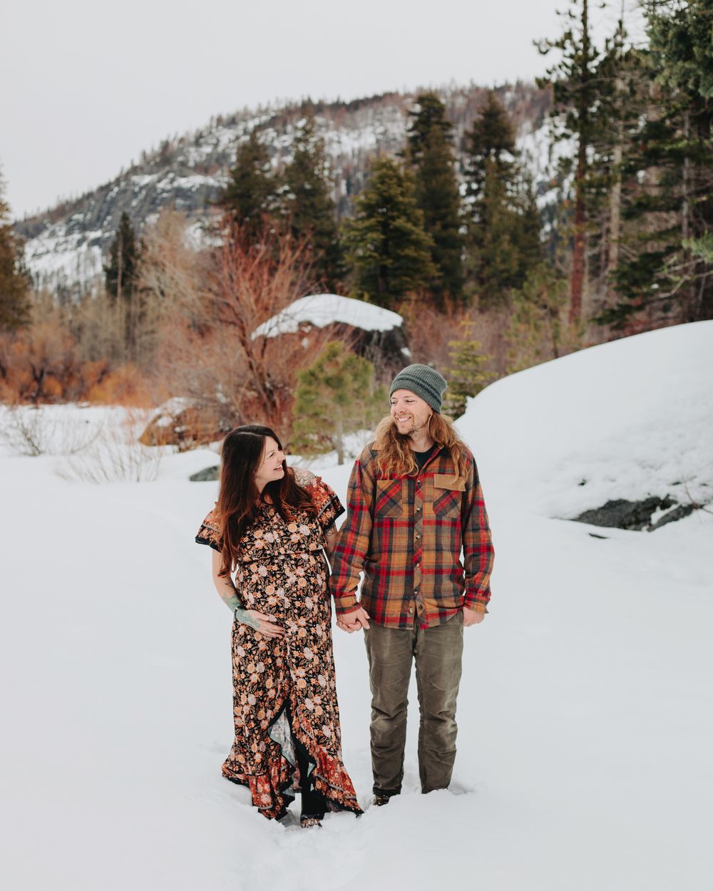 Expecting couple laughing in a snow covered meadow during a wintery mountain maternity shoot in Lake Tahoe