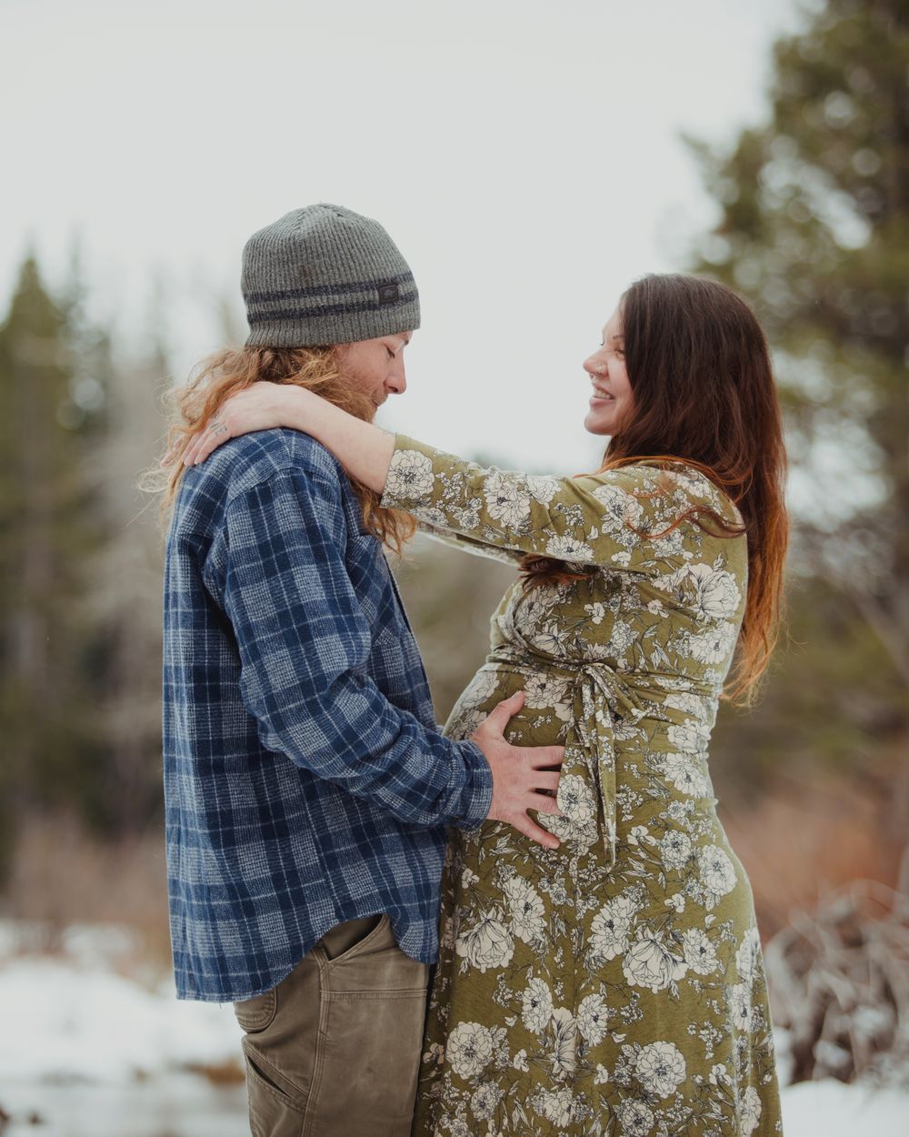 expecting couple embracing in the snowy mountains
