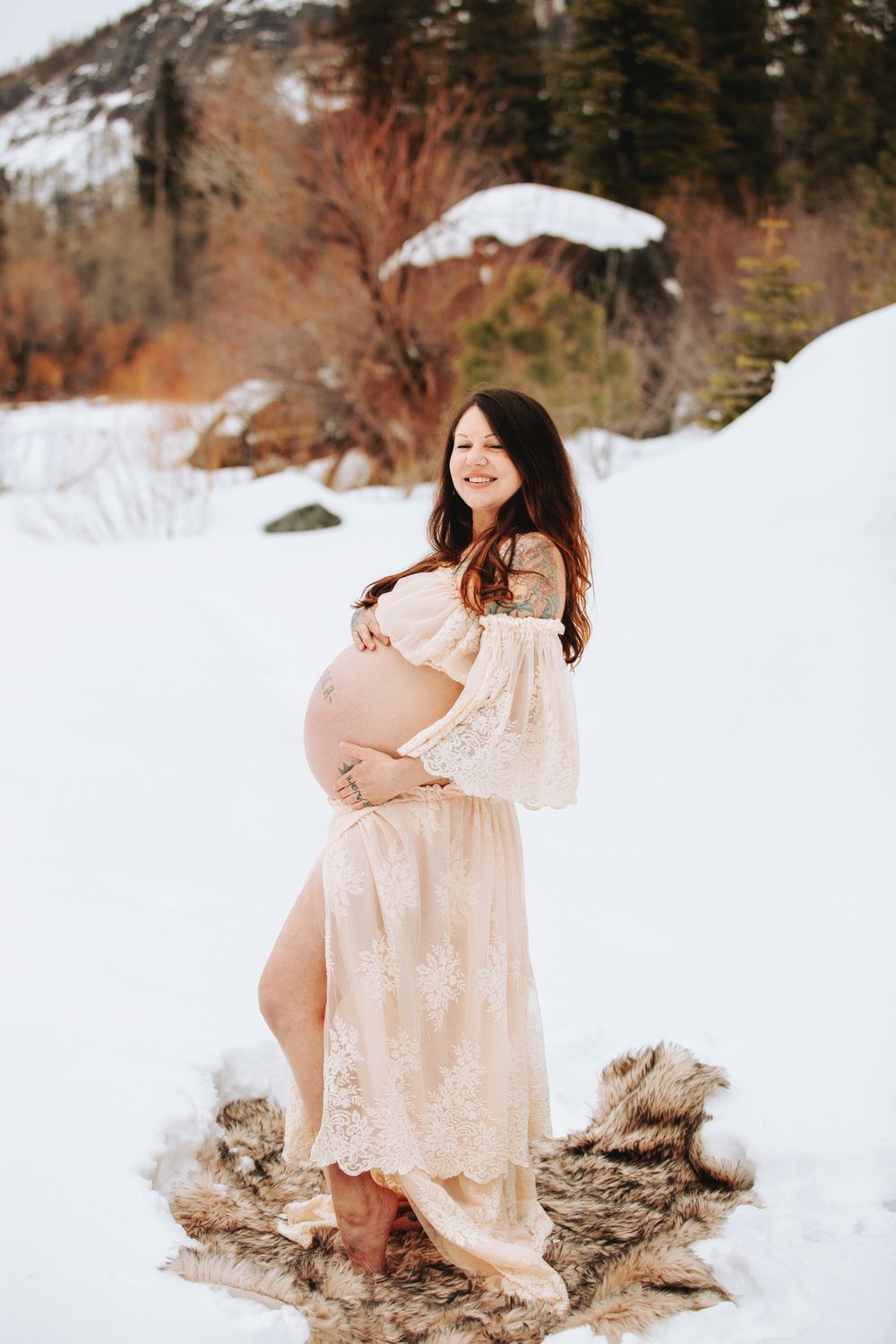 pregnant mom holding her bare belly in a snow covered meadow during a wintery mountain maternity shoot in Lake Tahoe
