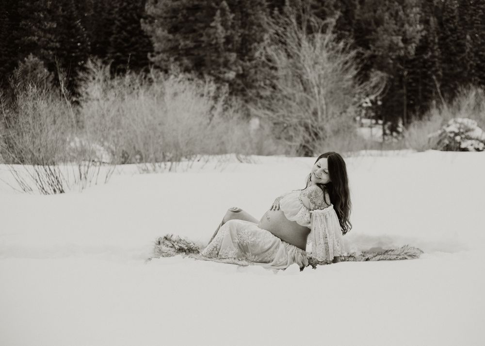 expecting mom sitting in a gown in a snow covered meadow during a wintery mountain maternity shoot in Lake Tahoe