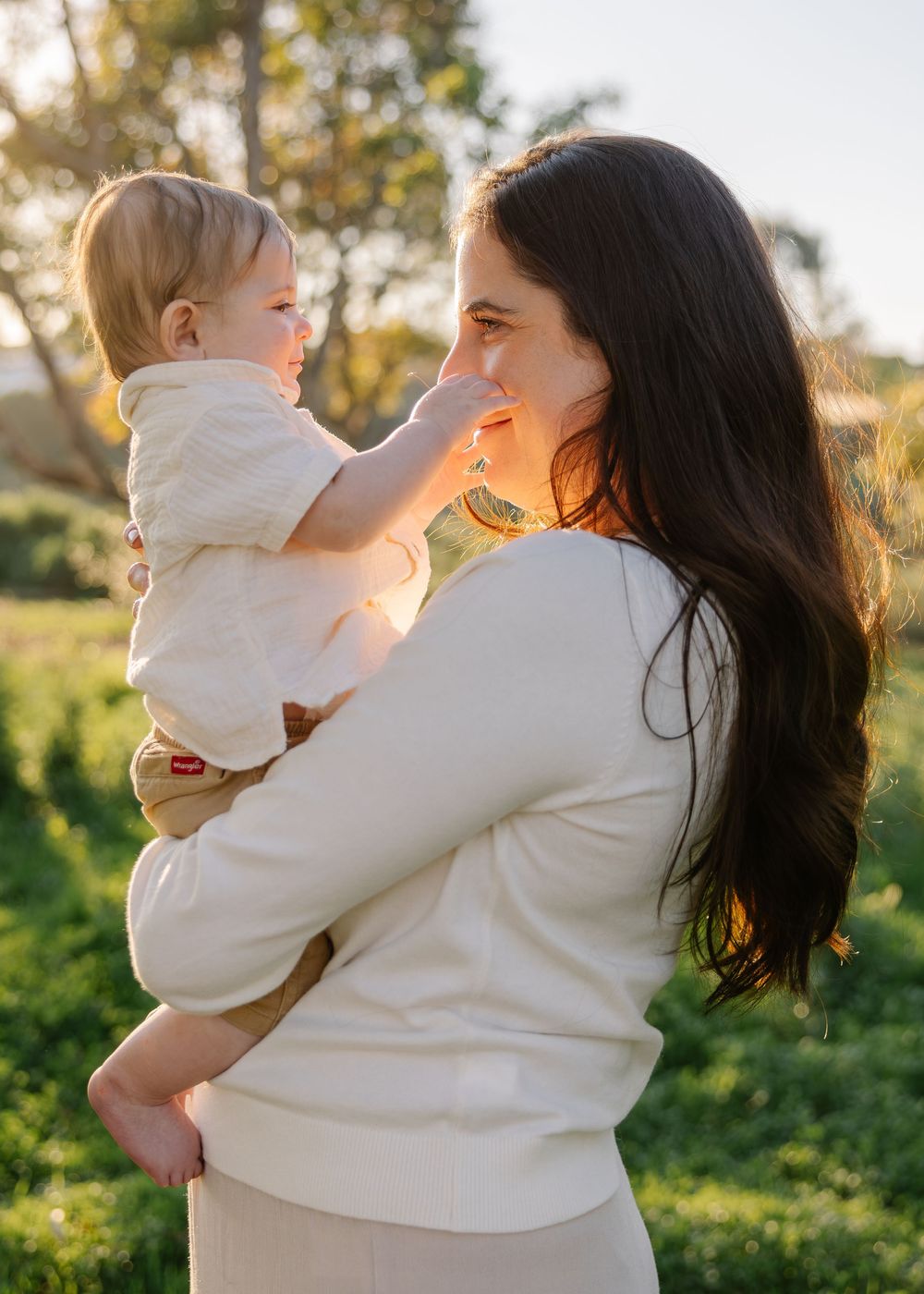 A tender moment captured in golden sunlight shows a parent and child embracing outdoors in white sweaters.
