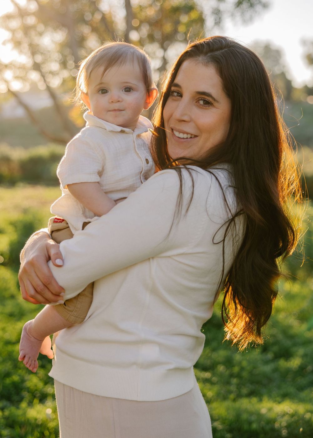 A parent and baby share joyful moments together during a golden hour photoshoot in a sunny outdoor setting.
