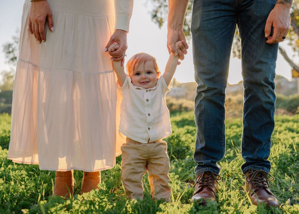 Family members' legs and feet are captured in a candid outdoor photo with natural sunlight filtering through.