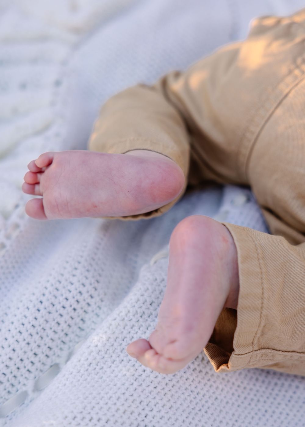Close-up of tiny baby feet resting on a white textured blanket in natural light.