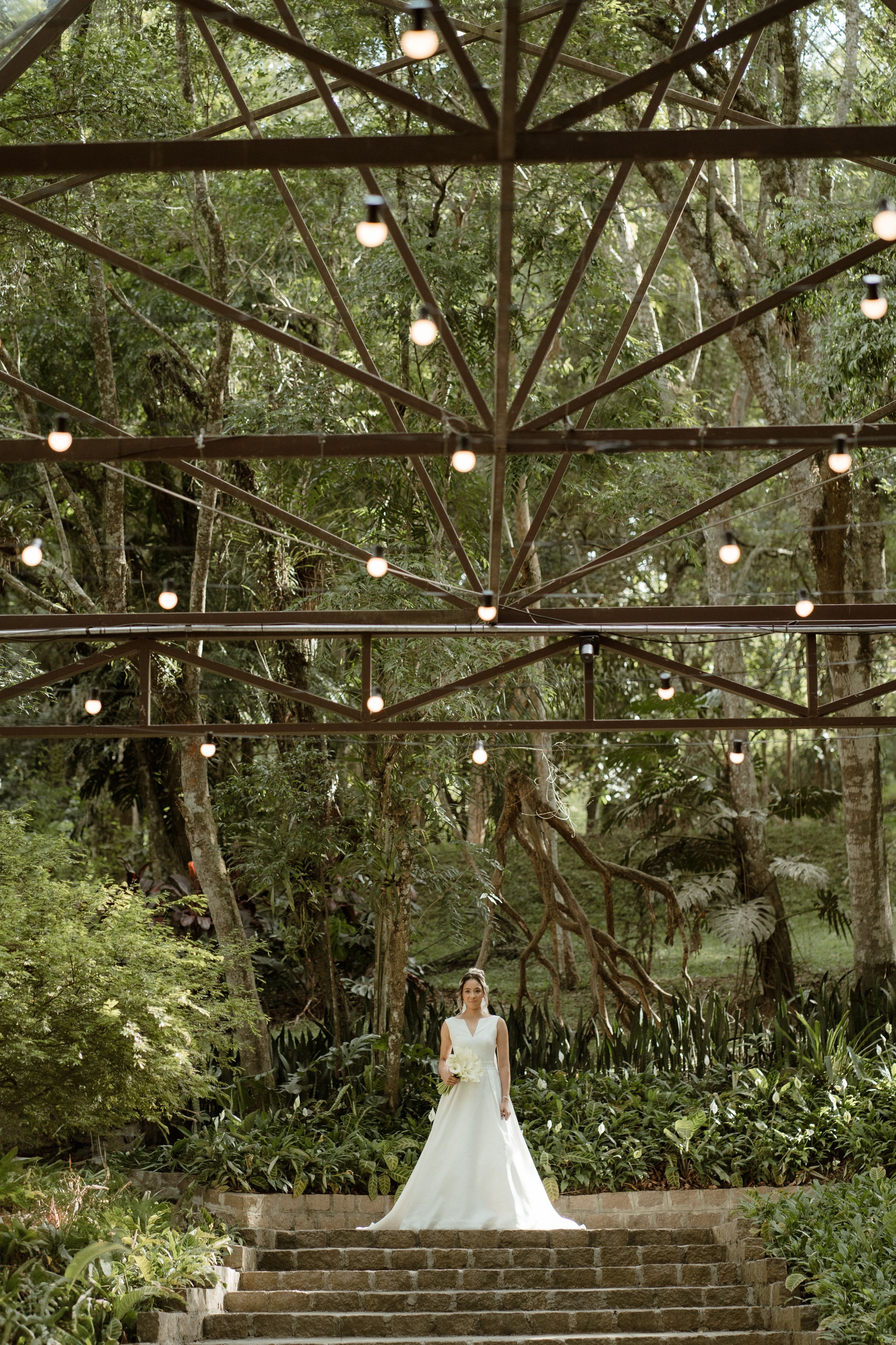 String lights illuminate a forested wedding venue with stone steps and white decorations.
