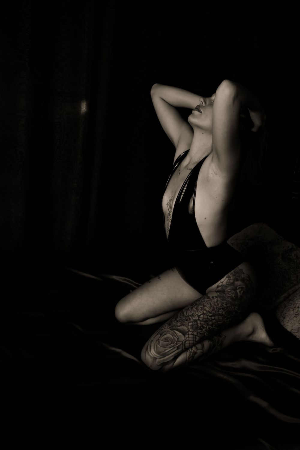 Artistic black and white boudoir photo showing silhouette in dark lingerie with visible tattoos.