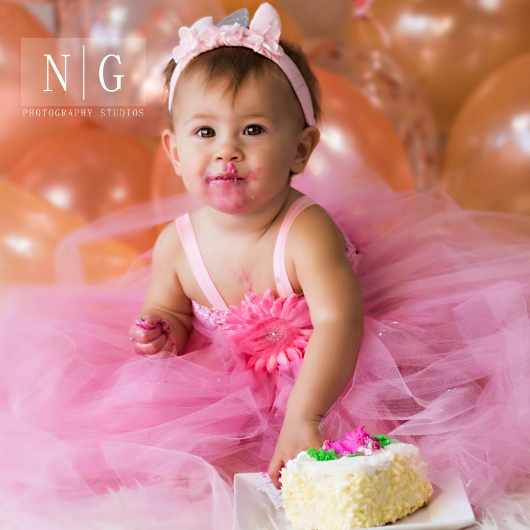 Baby in pink tutu dress having cake smash photo session with peach-colored backdrop.