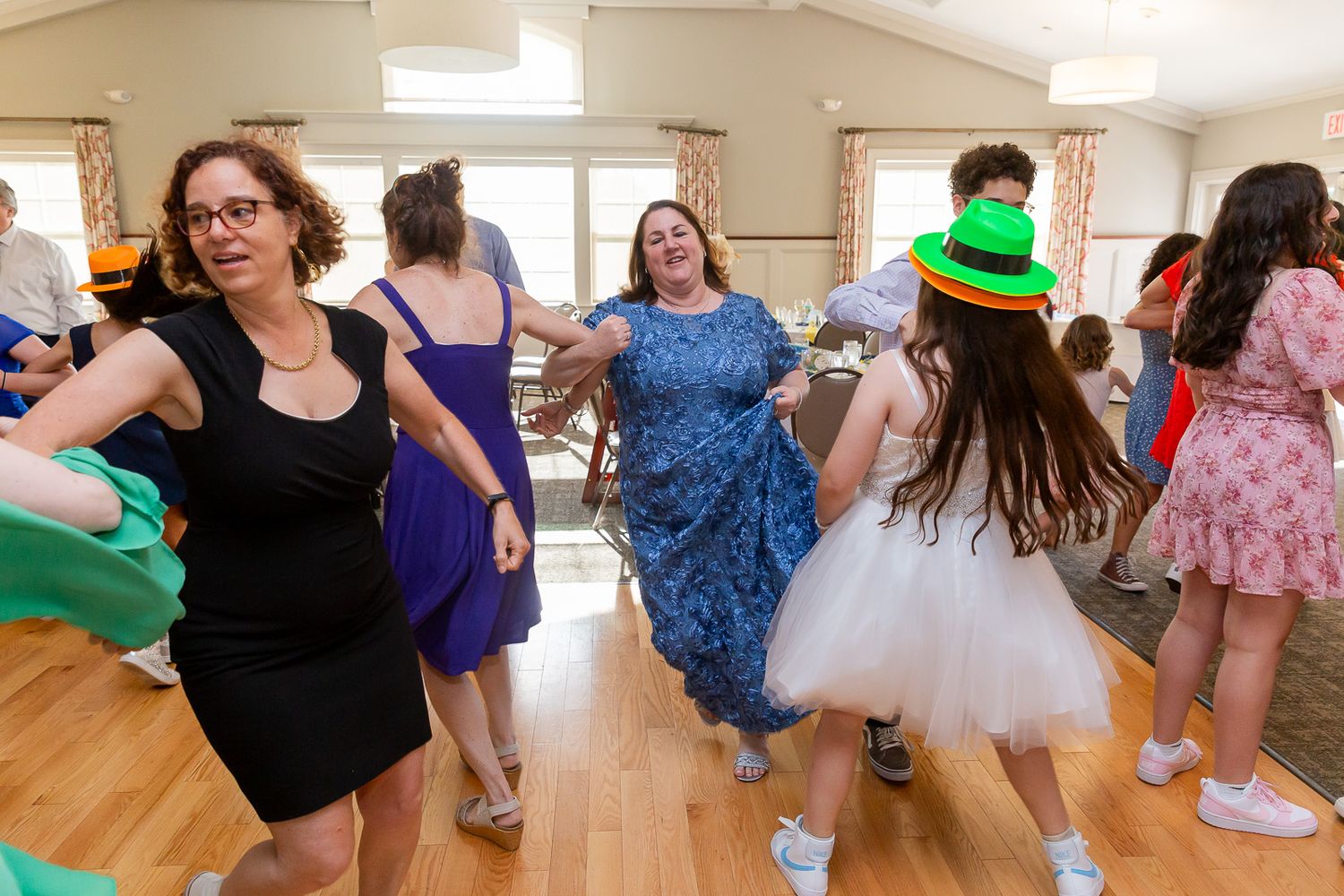 Celebrants dancing in formal wear and costumes during a festive party in a community hall.
