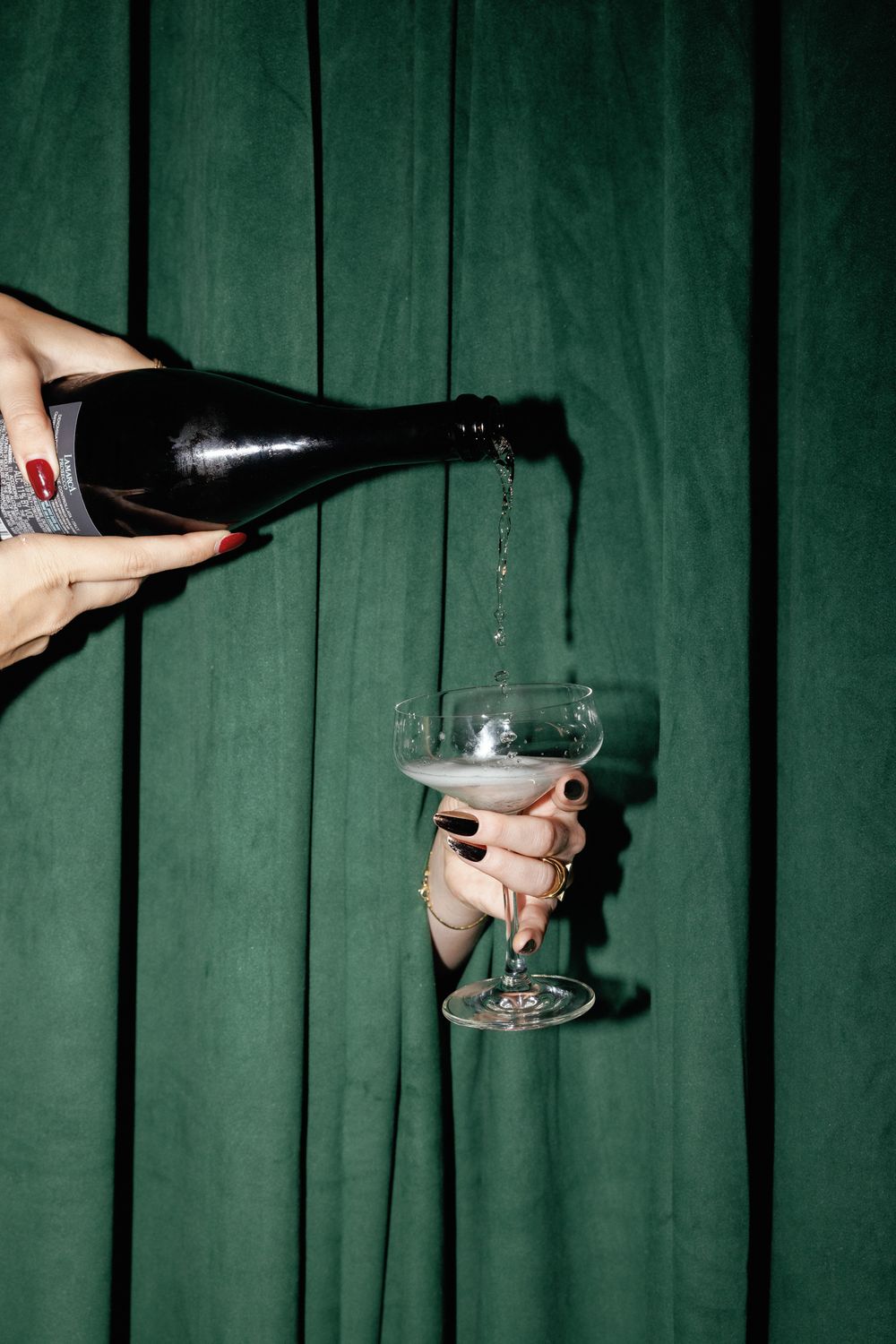 Champagne being poured into a glass against an emerald green curtain backdrop.