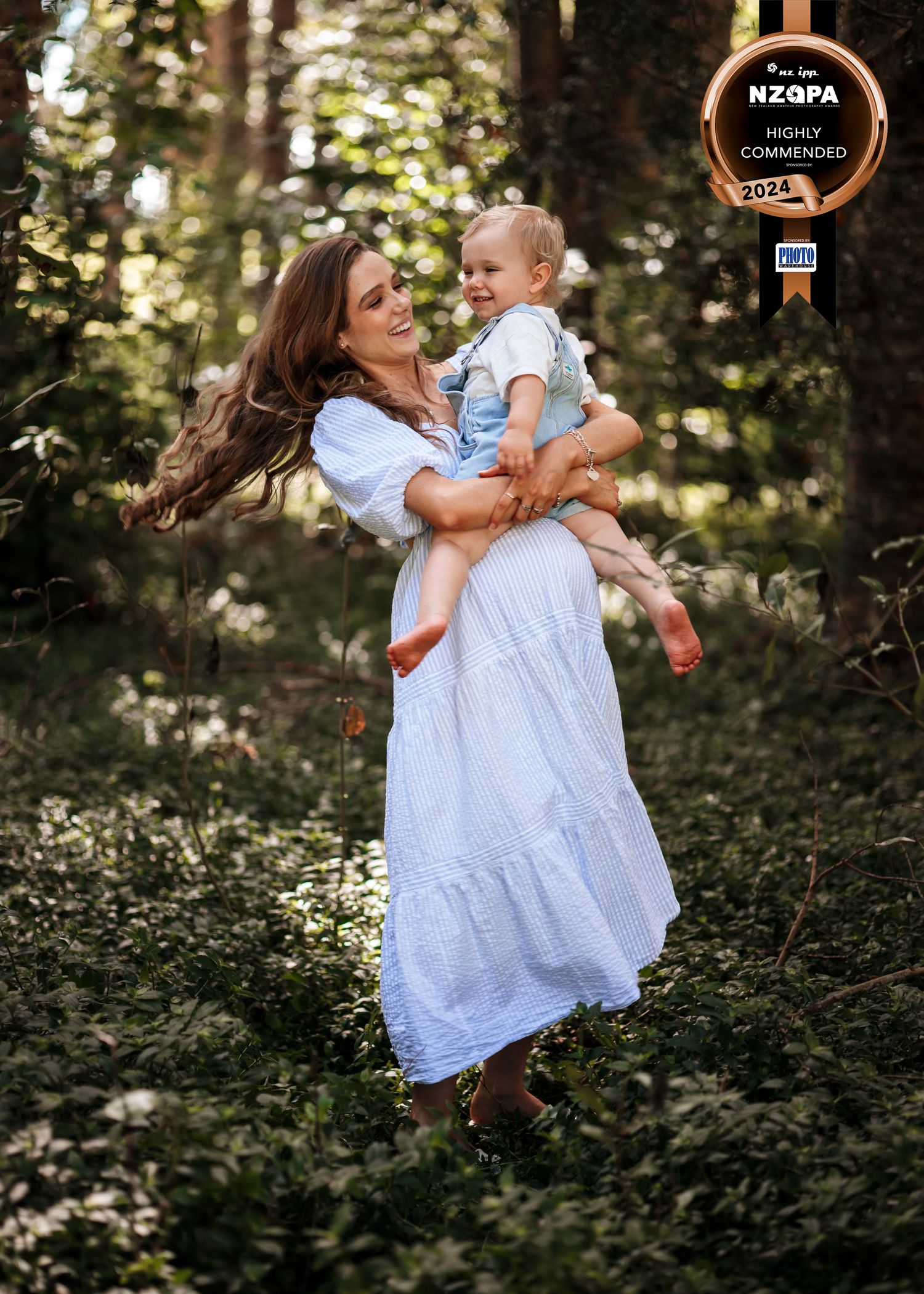 A mother and her young child playfully swinging around in a forest setting. CL Photography