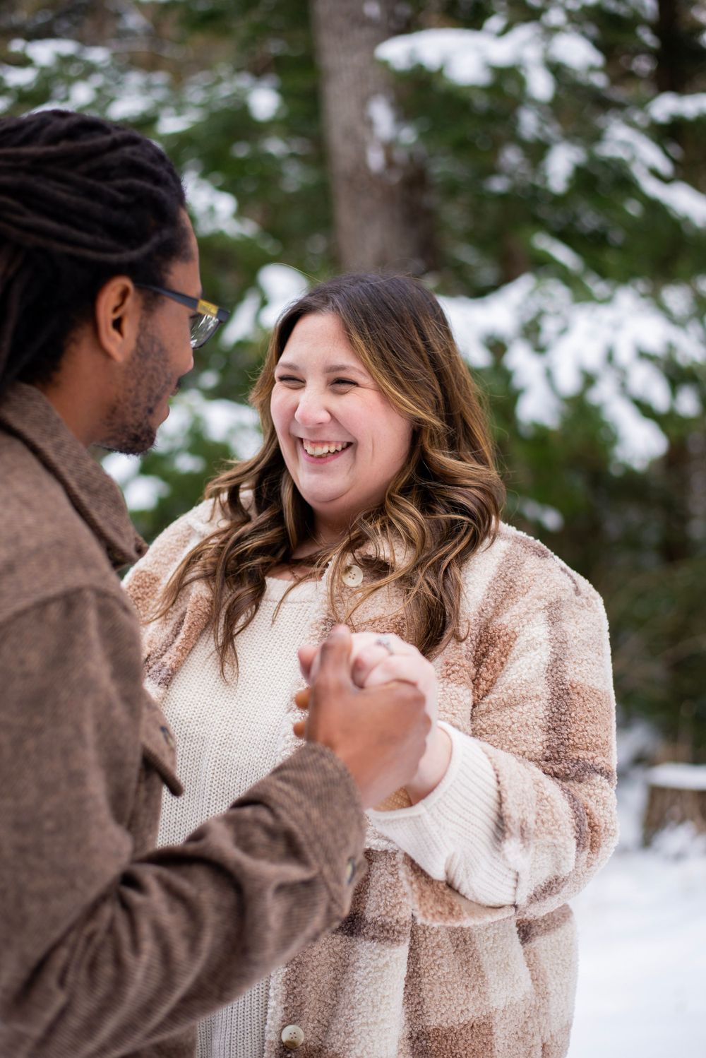 Two people share a joyful moment outdoors in a snowy winter setting, wearing cozy sweaters and jackets.