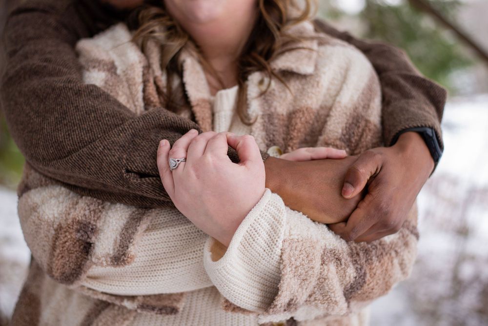 A close-up view of hands clasping together while wearing cozy cream and brown sweaters in winter.