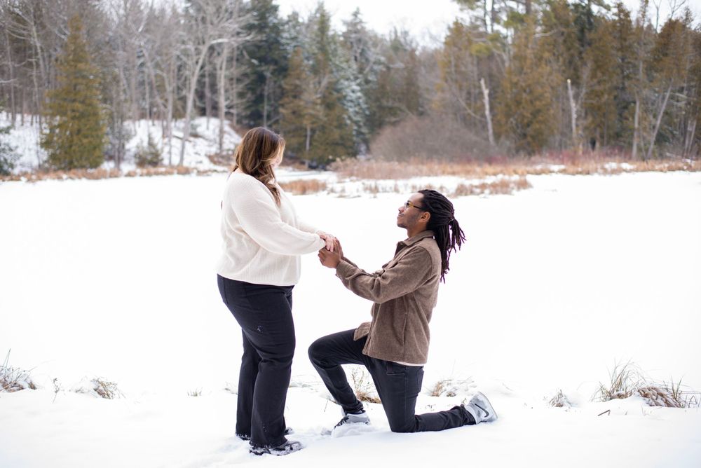 A romantic winter proposal scene with someone kneeling in front of their partner in a snowy landscape.
