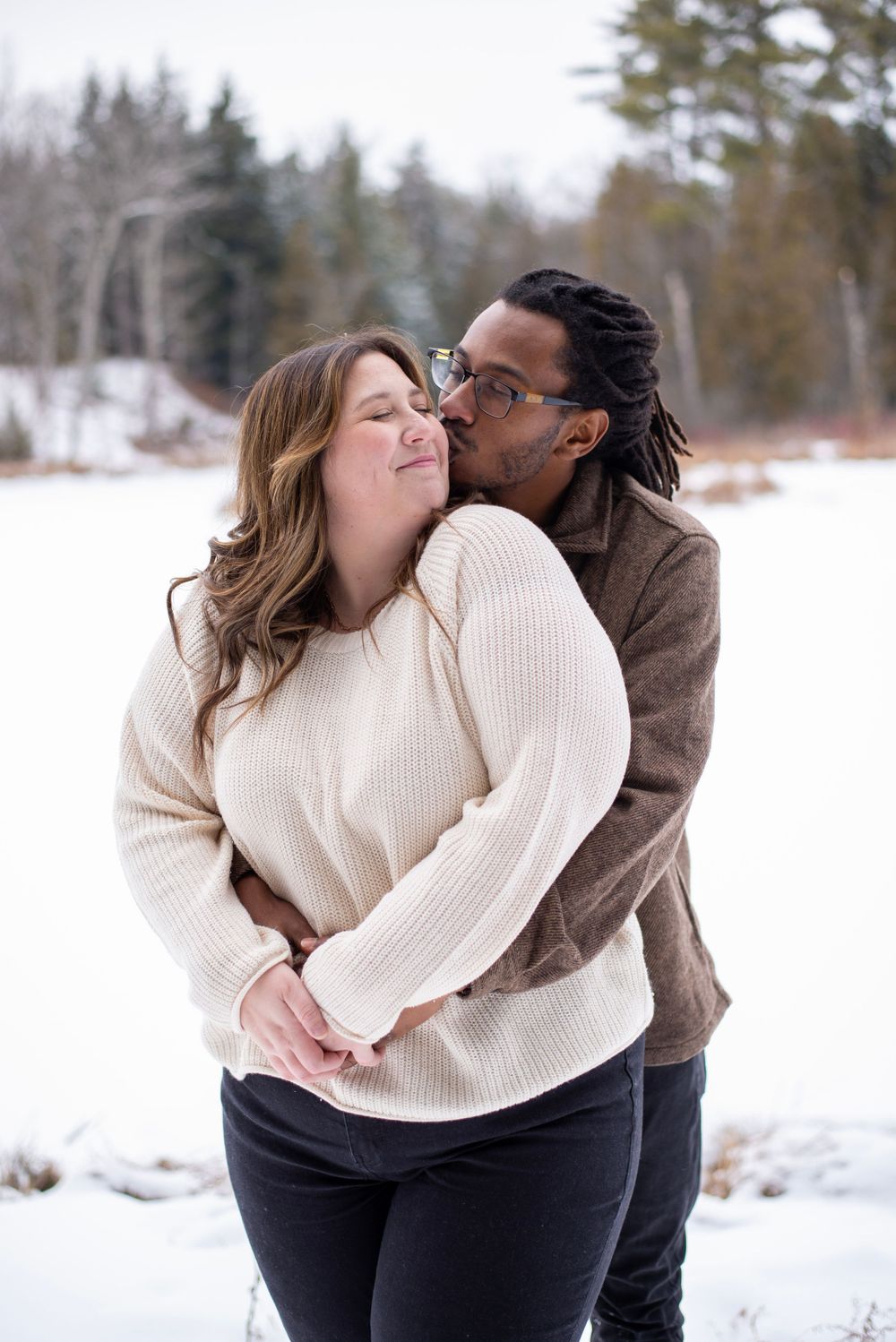 An interracial couple share an intimate moment together in a snowy winter setting wearing warm knitwear.