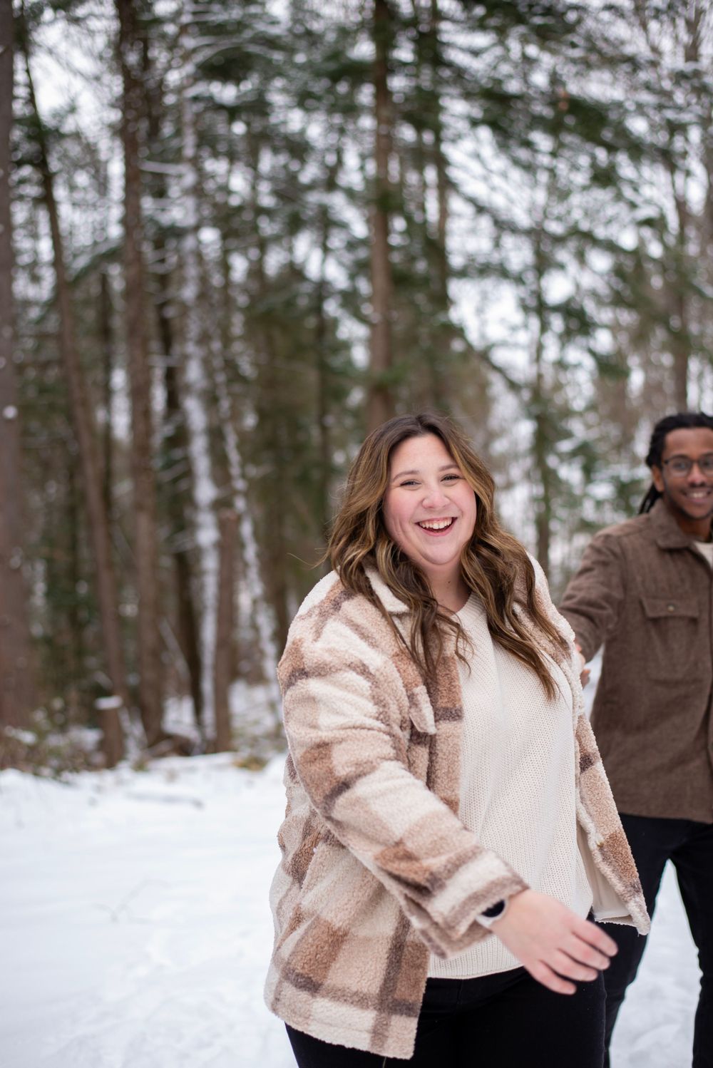 Two people enjoying a winter day in the snowy woods, wearing warm jackets against the cold forest backdrop.