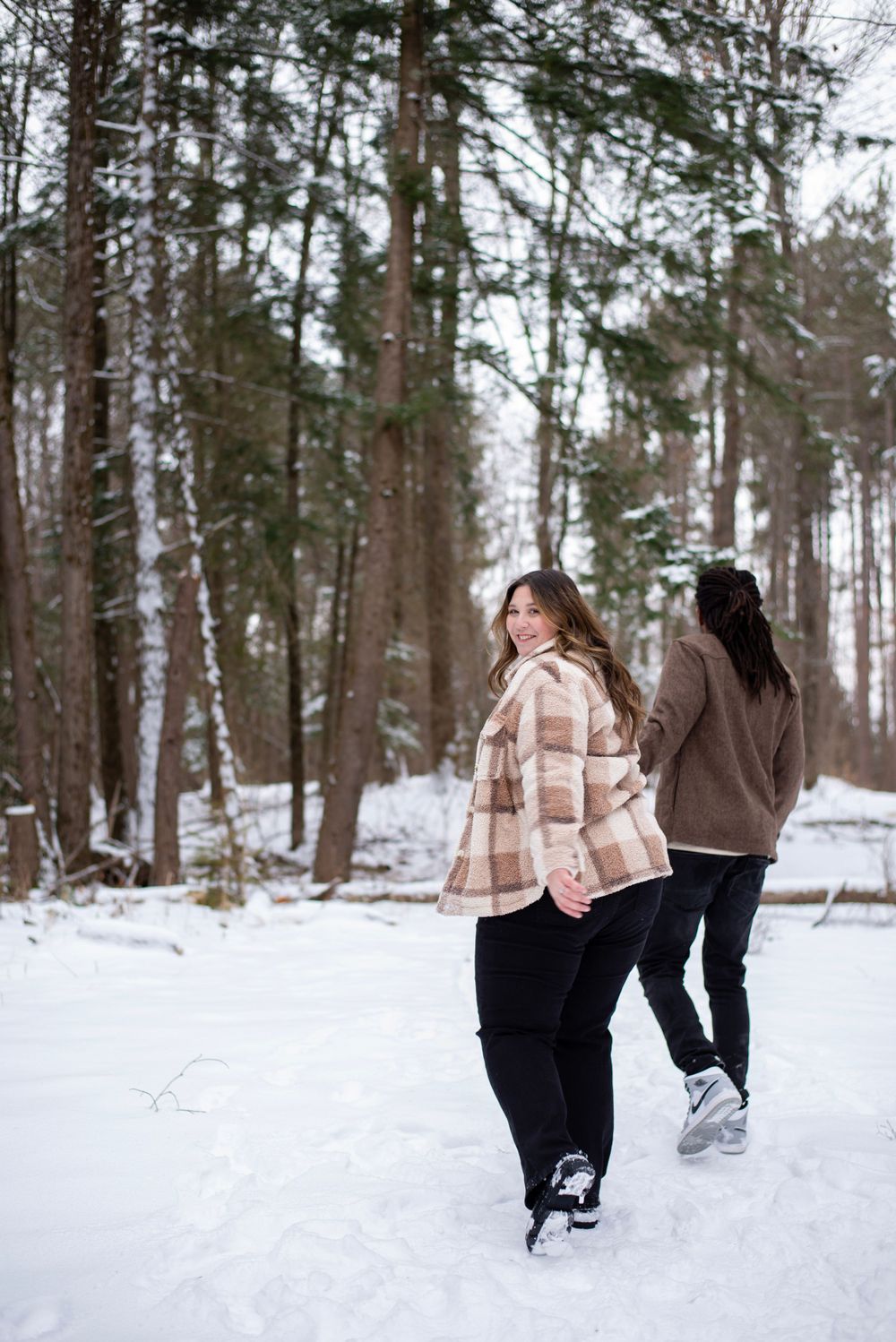 Two people enjoy a winter walk through snowy woods, wearing warm coats and boots on a cold winter day.