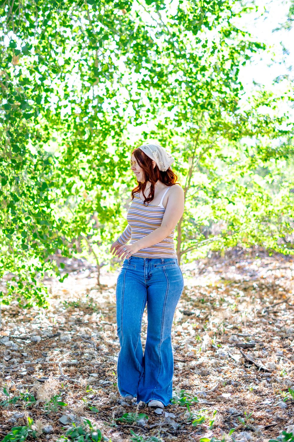 A casual outdoor portrait against green foliage wearing denim and a striped shirt.