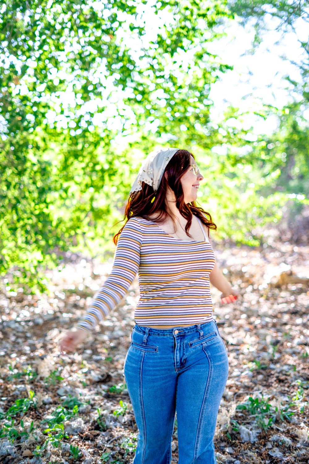 Side profile in striped shirt and jeans against green foliage background in natural lighting.